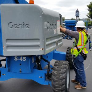 A person in a safety harness and hard hat working on a mobile elevated work platform