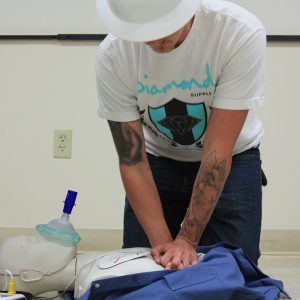A person kneeling on the floor while practicing chest compressions on a test dummy