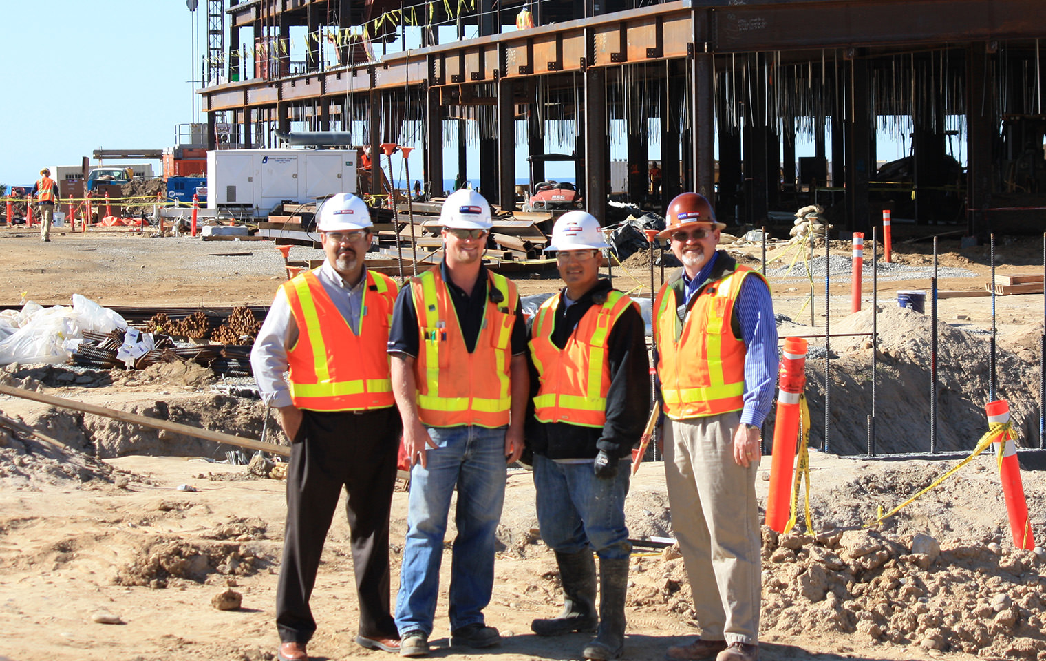 Four people in high visibility vests and hard hats standing outside at a construction site