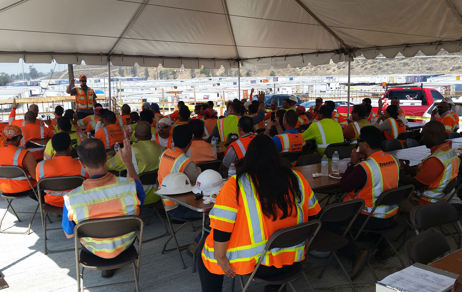 A large group of people in high visibility vests sitting under a tent while participating in a training event